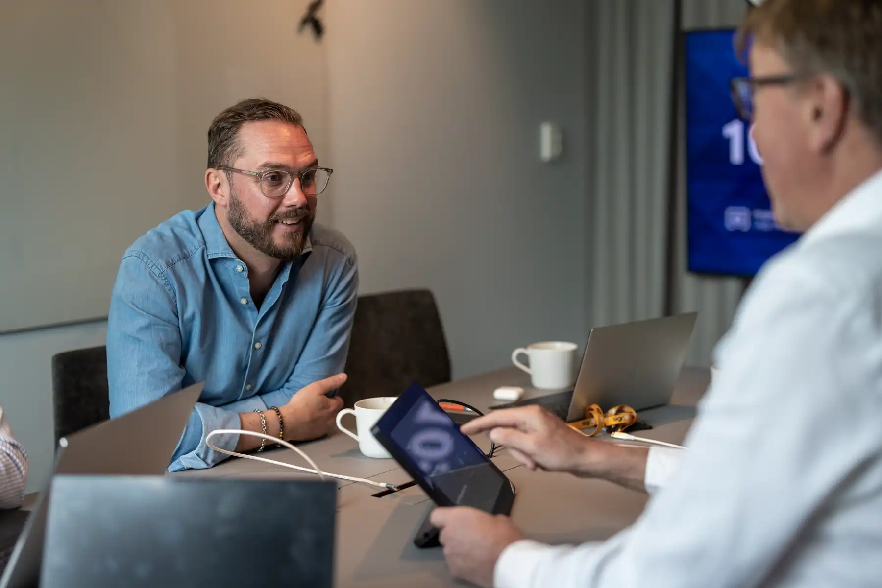 Two colleagues in a meeting, one using a tablet.