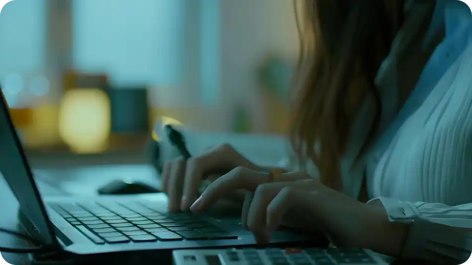 Close-up of hands typing on a laptop, with a calculator visible below.