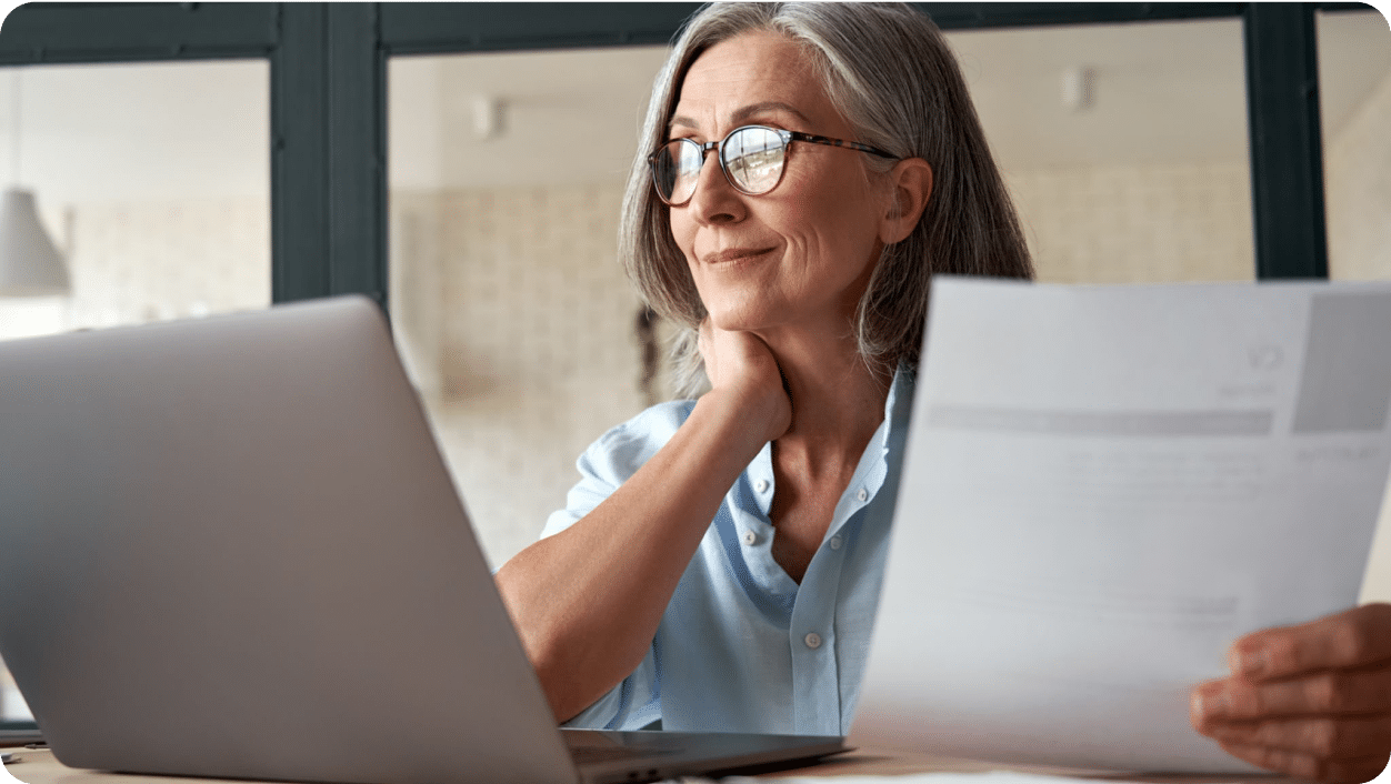 A woman looking thoughtfully at a laptop and documents.