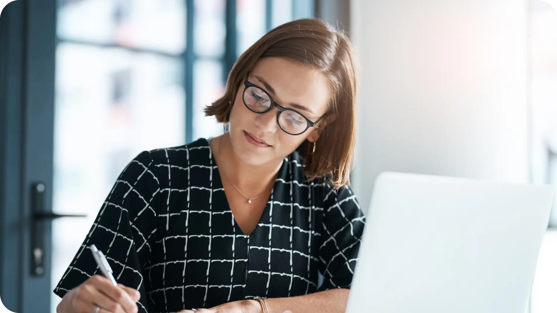 Woman in glasses sitting in front of a laptop writing on paper