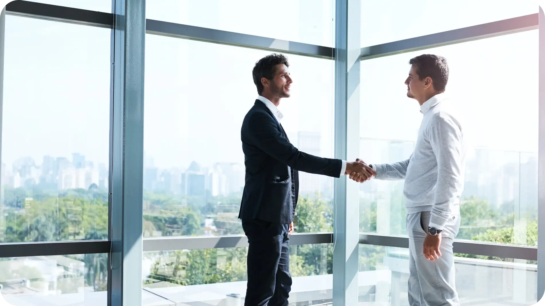 Two business men shaking hands in front of big windows.