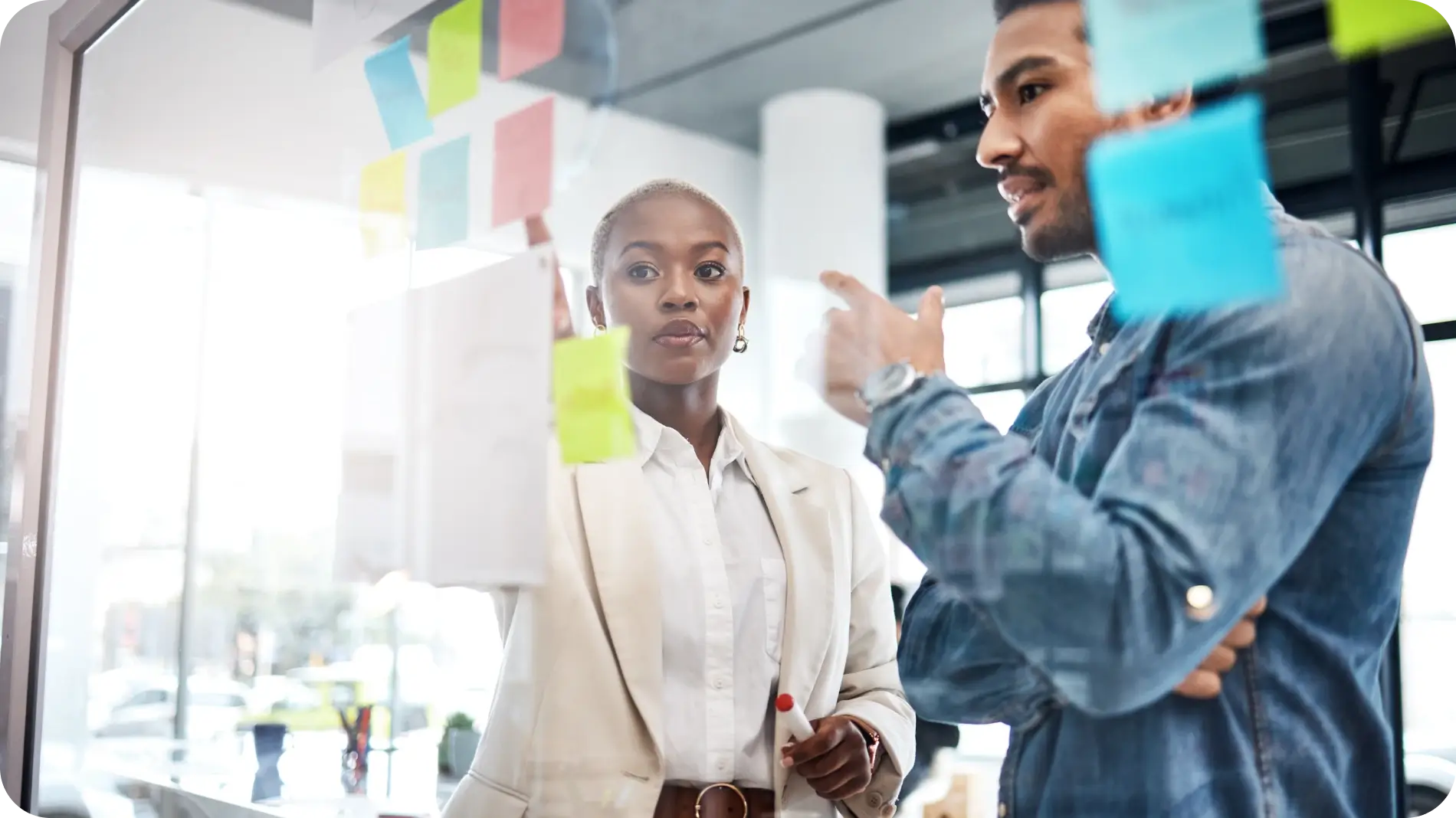 A woman and man standing in front of a whiteboard with post-its.
