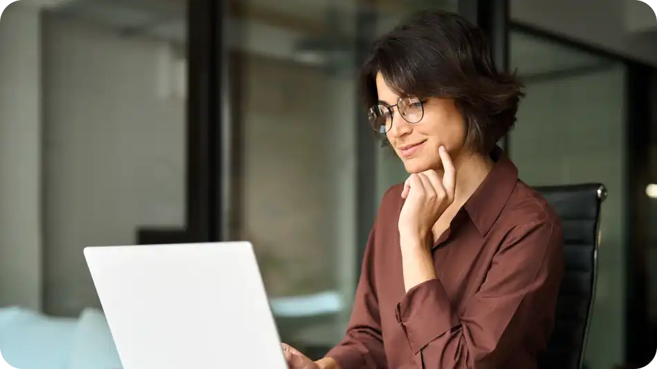Business woman wearing glasses, sitting in front of laptop smiling.