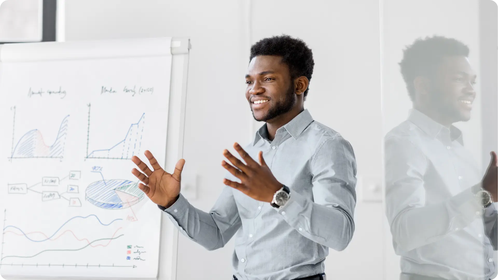 A man is smiling and gesturing while giving a presentation in front of a flip chart with graphs.
